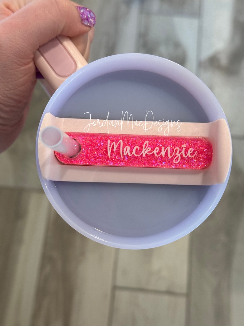 Puede incluir: Un vaso rosa y blanco con una tapa de purpurina rosa y una pajita. La tapa tiene un inserto de purpurina rosa con el texto "Jordan Mae Designs Mackenzie" en &eacute;l.