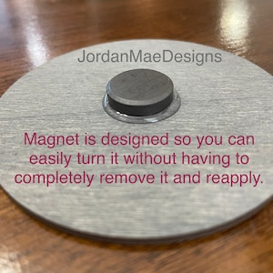 Peut inclure: Une plaque ronde en bois gris avec le texte "JordanMaeDesigns" et les mots "Magnet is designed so you can easily turn it without having to completely remove it and reapply." Un aimant rond noir est fix&eacute; &agrave; la plaque.