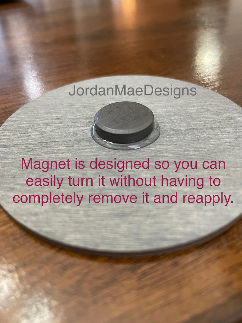 Peut inclure: Une plaque ronde en bois gris avec le texte "JordanMaeDesigns" et les mots "Magnet is designed so you can easily turn it without having to completely remove it and reapply." Un aimant rond noir est fix&eacute; &agrave; la plaque.