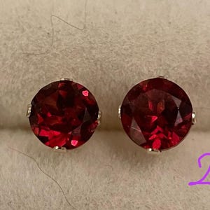 May include: A pair of red gemstone earrings with silver settings. The earrings are round and have a shiny finish.