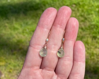 May include: A pair of gold earrings with a teardrop-shaped green gemstone and a small diamond accent.