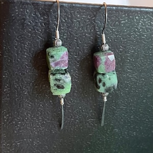 May include: A pair of silver earrings with two green and purple gemstone beads on each earring.