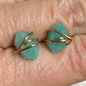 May include: A pair of earrings featuring a light green gemstone wrapped in gold wire.