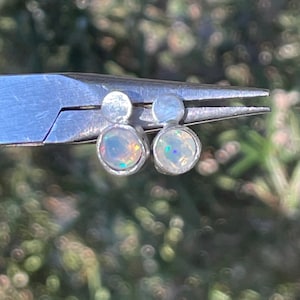 May include: A pair of silver stud earrings with small, round, iridescent opal stones.