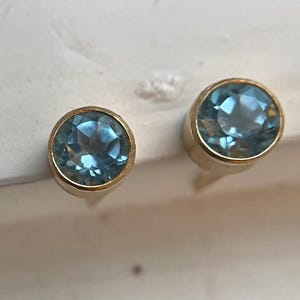 May include: A pair of gold earrings with blue gemstones. The earrings are round and have a simple design.