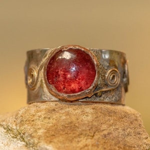 May include: A silver ring with a red gemstone set in copper. The ring has a textured band with wire details.