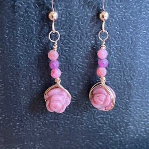 May include: A pair of dangle earrings with pink rose quartz flowers and pink beads. The earrings are made with gold-toned wire.