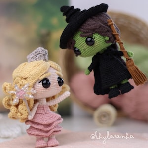 Pode incluir: Duas bonecas de crochê: uma princesa com um vestido rosa e uma bruxa com roupa preta. A princesa tem cabelo loiro e uma coroa prateada. A bruxa tem pele verde, um chapéu preto e uma vassoura. As bonecas são feitas à mão.