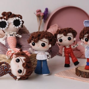 Puede incluir: Colección de muñecas de ganchillo hechas a mano, con cabello castaño y varios atuendos. Una muñeca es una sirena, otras visten vaqueros azules, monos rojos y un vestido azul. Las muñecas se exhiben con hilo y una bandeja decorativa.