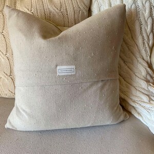 May include: A beige throw pillow with a white label that reads "The Stationery Shoppe". The pillow is made of a textured fabric and has a subtle sheen.