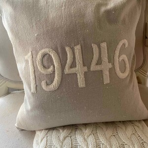 May include: A beige throw pillow with the number 19446 embroidered in white on the front.