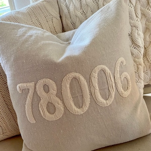 May include: A beige throw pillow with the number 78006 embroidered in white on the front.