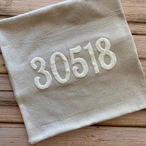 May include: A beige linen pillow with the number 30518 embroidered in white.