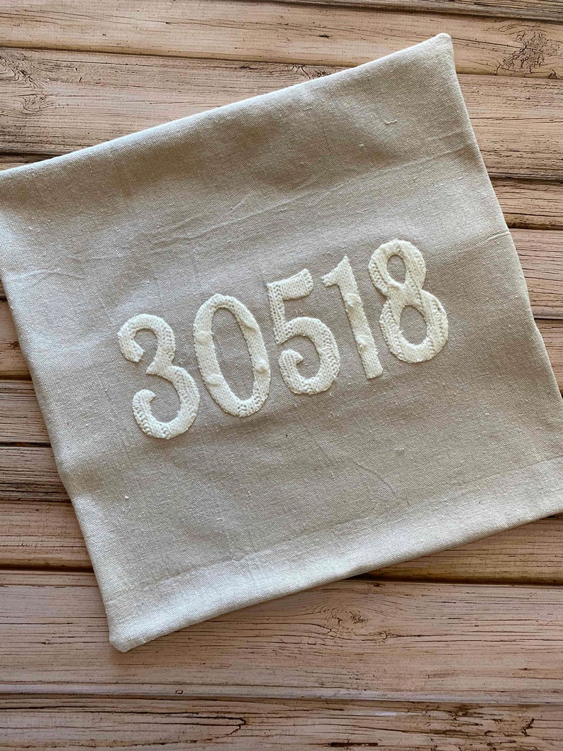 May include: A beige linen pillow with the number 30518 embroidered in white.