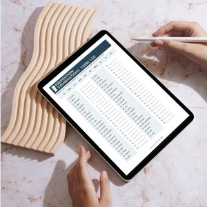 Può includere: Un tablet digitale che mostra un foglio di lavoro intitolato "Combinazioni di preposizioni: Verbi 1-50". Il foglio di lavoro è una guida allo studio della grammatica inglese. Un pezzo decorativo in legno è a sinistra.