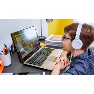 May include: A young person wearing headphones and glasses sits at a desk in front of a laptop computer. The laptop screen shows a video call with another person. The desk is cluttered with school supplies, including a basketball, pencils, and notebooks.