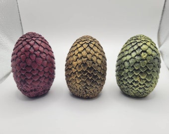May include: Three dragon egg-shaped figurines, one red, one gold, and one green. The figurines are made of a textured material that resembles scales.