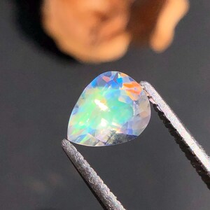 Op de afbeelding: Een peervormige, iriserende edelsteen met een regenboog aan kleuren, vastgehouden in een pincet.