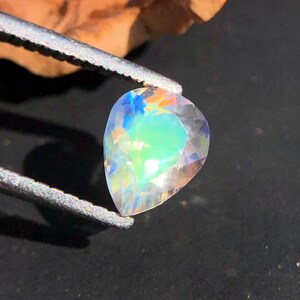 Op de afbeelding: Een peervormige, iriserende edelsteen met een regenboog van kleuren, waaronder blauw, groen en roze.