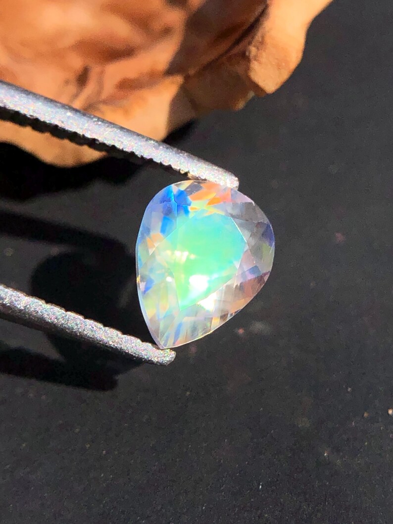 Op de afbeelding: Een peervormige, iriserende edelsteen met een regenboog van kleuren, waaronder blauw, groen en roze.