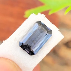 May include: A dark blue, rectangular, faceted gemstone on a white surface.