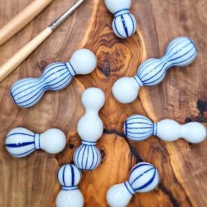 May include: A collection of eight white ceramic gourds with blue and white striped designs. The gourds are arranged on a wooden surface.