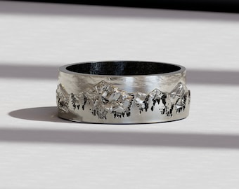 Puede incluir: Un anillo de plata con un diseño de cordillera. El anillo es ancho y tiene una superficie texturizada.