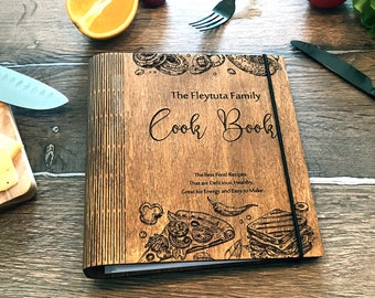 May include: A wooden cookbook with a black elastic band closure. The cover is engraved with the text "The Fleytuta Family Cook Book" and a design of pizza and sandwiches. The text below the title reads "The Best Food Recipes That are Delicious, Healthy, Great for Energy and Easy to Make."