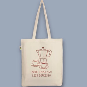 Könnte beinhalten: Beige Canvas-Tragetasche mit einer roten Strichzeichnung einer Kaffeemaschine und zwei Kaffeetassen. Der Text "MORE ESPRESSO LESS DEPRESSO" ist darunter gedruckt. Die Tasche hat zwei lange Griffe.