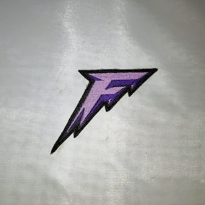 May include: Embroidered patch featuring a stylized purple letter "F" within a black outline, shaped like a lightning bolt. The patch is on a light gray background. The design is simple and bold.