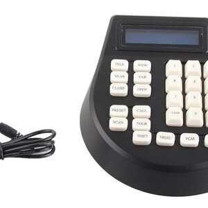 May include: A black security camera controller featuring a joystick, a numeric keypad with white buttons, and an LCD screen. The device includes a black power adapter with a cord. The buttons are labelled with text including TELE, WIDE, NEAR, FAR, CLOSE, OPEN, PRESET, CALL, SCAN, TOUR, SHIFT, MENU, PGM, AUX, CAM, and numbers 0 through 9.