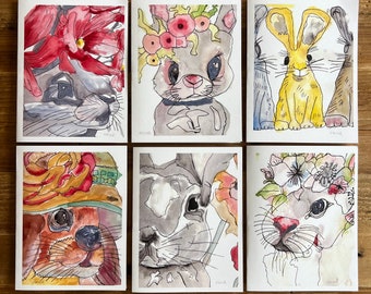 May include: Six watercolor paintings on white cardstock featuring different animals wearing floral crowns. The animals include a rabbit, a cat, and a dog.