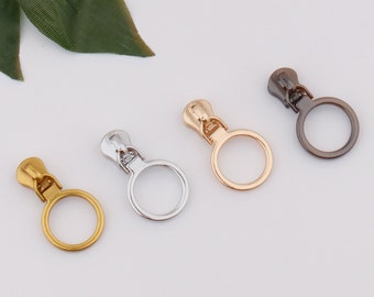 May include: Four zipper pulls in different finishes: silver, gold, rose gold, and gunmetal. Each pull has a round loop.