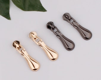 May include: Two pairs of zipper pulls, one pair in gold and one pair in black. The pulls are teardrop shaped with a decorative design.