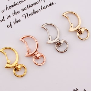 Pode incluir: Quatro chaveiros de metal em forma de lua crescente, nas cores prata, ouro e ouro rosa, com fecho giratório.