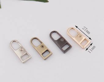 Może przedstawiać: Cztery metalowe breloki w różnych wykończeniach: srebrny, brązowy, czarny i złoty. Każdy brelok ma 27 mm długości i 11 mm szerokości.