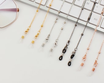 May include: Five different colored chains with clear clasps on each end. The chains are laid out on a white keyboard with black keys. The chains are gold, silver, black, rose gold, and a lighter shade of gold.