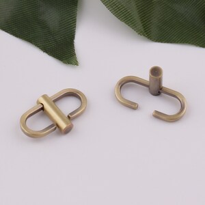 Op de afbeelding: Twee antieke gouden metalen draaibare sluitingen, elk met een enkele lus en een verbindingsstang. De sluitingen zijn ideaal voor het bevestigen van banden of kettingen aan tassen, handtassen of andere accessoires.