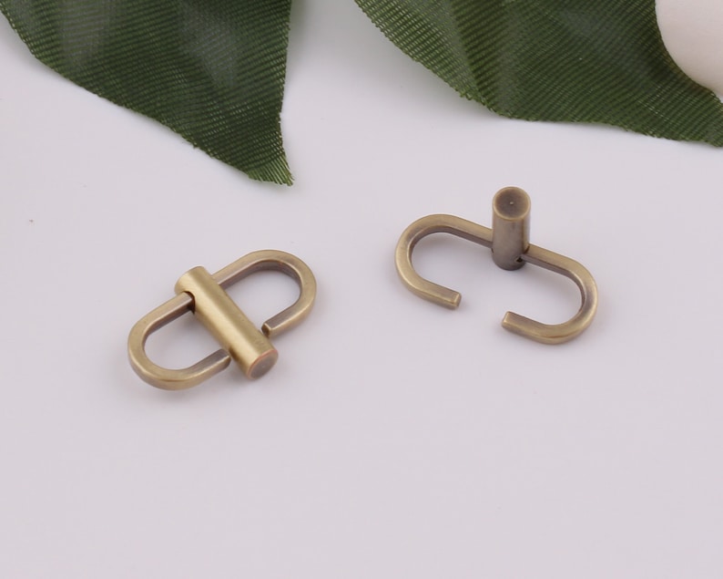 Op de afbeelding: Twee antieke gouden metalen draaibare sluitingen, elk met een enkele lus en een verbindingsstang. De sluitingen zijn ideaal voor het bevestigen van banden of kettingen aan tassen, handtassen of andere accessoires.