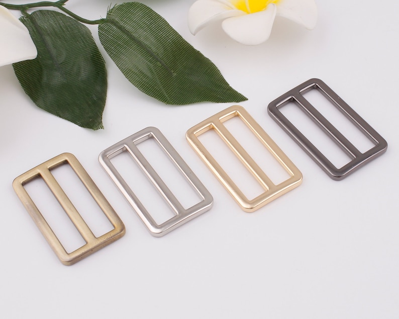 May include: Four metal slider buckles in different finishes: antique brass, silver, gold, and gunmetal. Each buckle is rectangular with two parallel slots.