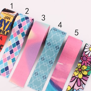 May include: Six different patterned fabric ribbon trims. The trims are pink, blue, and white with various patterns including geometric shapes, flowers, and a newspaper print.