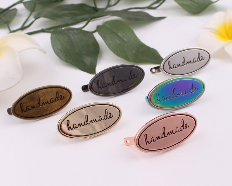 May include: Six oval-shaped metal tags with the word "handmade" inscribed on each. The tags are in various finishes, including silver, gold, bronze, and iridescent.