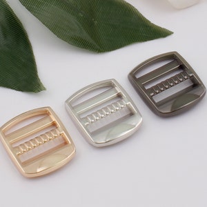 Puede incluir: Tres hebillas deslizantes de metal en dorado, plateado y negro.