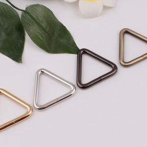 May include: Four triangle-shaped metal rings in gold, silver, black, and bronze. The rings are about 2 inches in diameter.