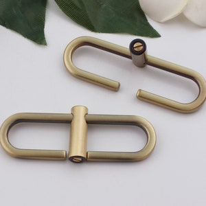 May include: Two antique gold metal oval-shaped clasps with a screw closure. The clasps are open and ready to be attached to a strap or other item.