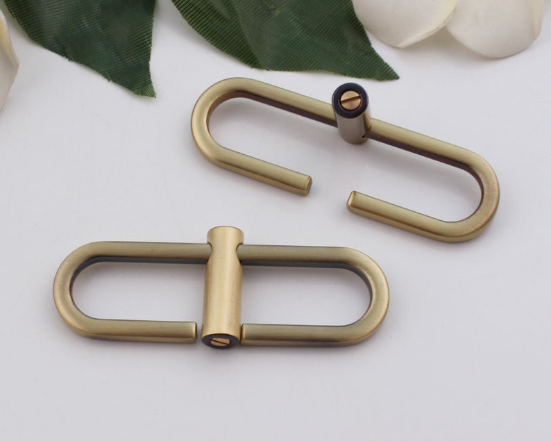 May include: Two antique gold metal oval-shaped clasps with a screw closure. The clasps are open and ready to be attached to a strap or other item.