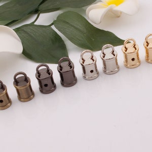 Può includere: Sette tappi metallici a forma di barile in diverse finiture: oro, argento, bronzo e nero. Ogni tappo ha un piccolo anello nella parte superiore.