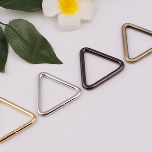 Może przedstawiać: Cztery metalowe pierścienie w kształcie trójkąta w różnych rozmiarach i wykończeniach: złote, srebrne, czarne i brązowe. Te pierścienie idealnie nadają się do mocowania do toreb, breloków lub innych akcesoriów.