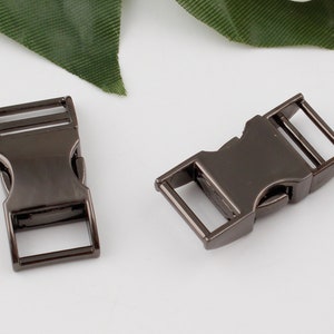 Op de afbeelding: Twee zwarte metalen zij-ontgrendelingsgespen. De gespen zijn gemaakt van metaal en hebben een matte afwerking.