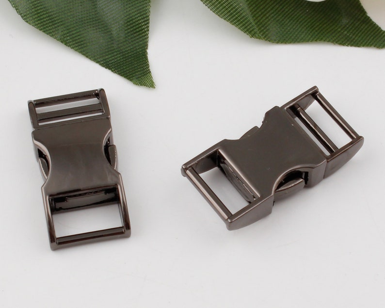 Op de afbeelding: Twee zwarte metalen zij-ontgrendelingsgespen. De gespen zijn gemaakt van metaal en hebben een matte afwerking.